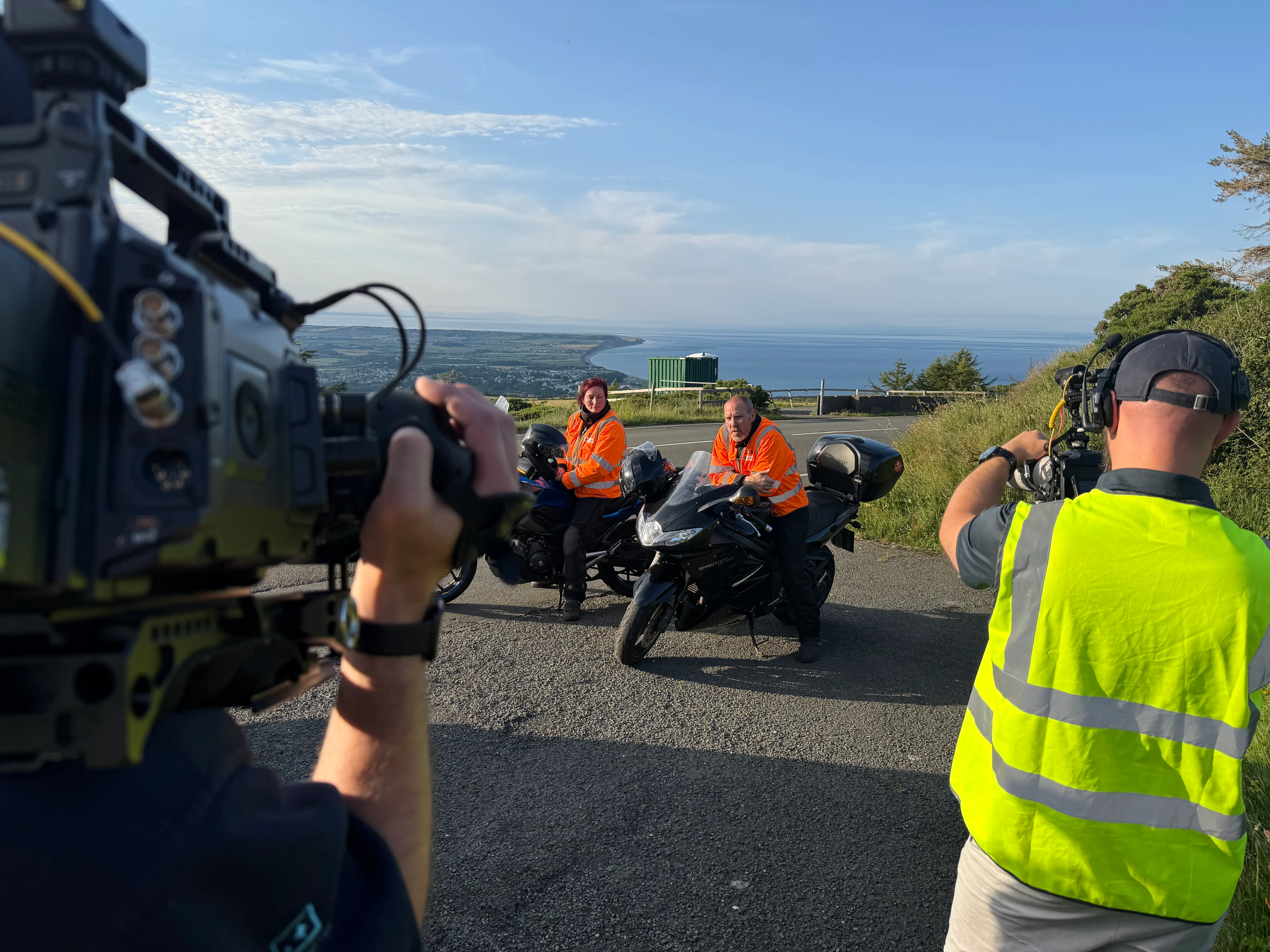 Will Oates and Nico van Loggerenberg filming two Chief Sector Marshals in Sector 9 on a coastal hillside road on the Isle of Man