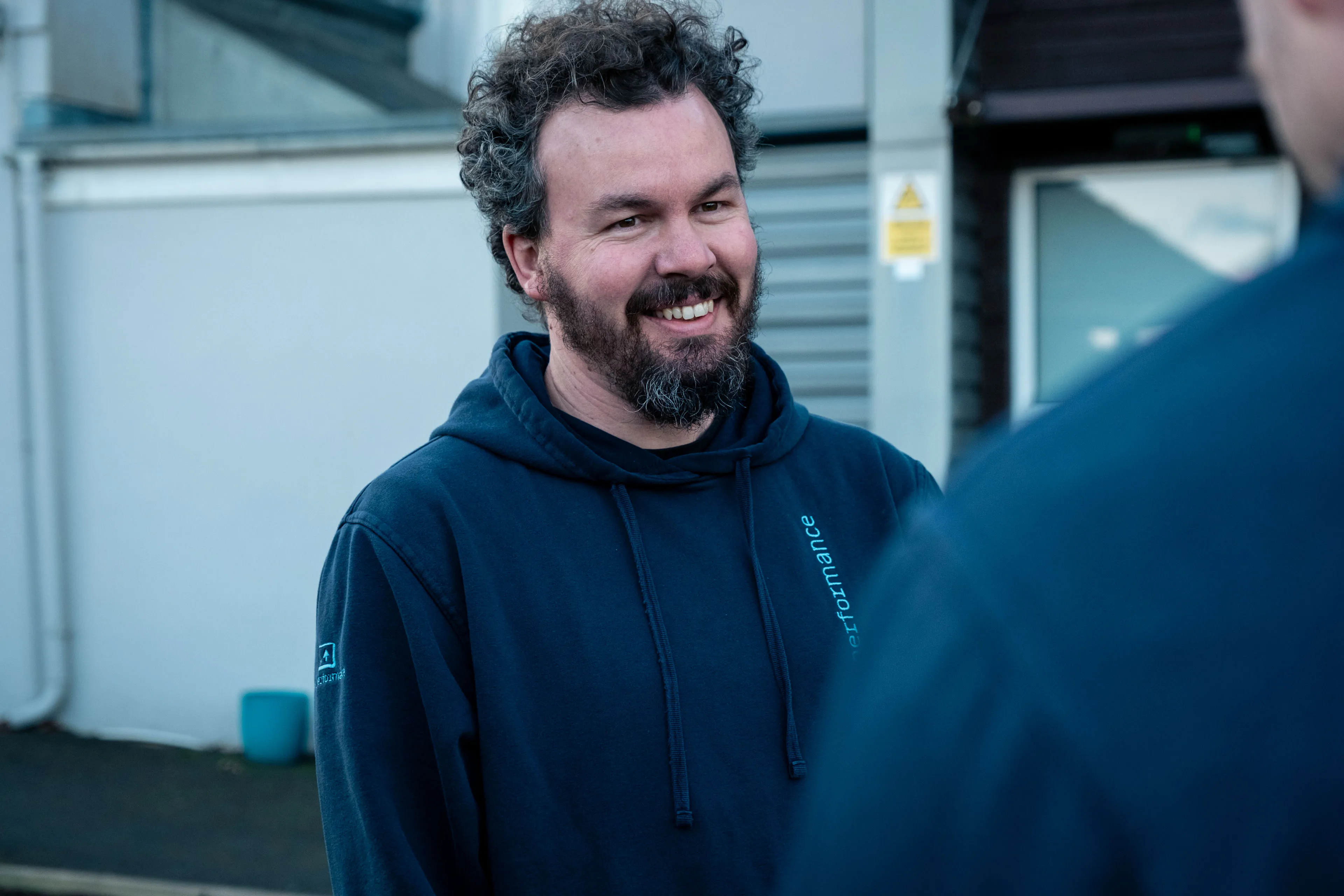Adrian Crellin talking with a colleague outside DotPerformance in the Isle of Man, wearing a DotPerformance hoodie.