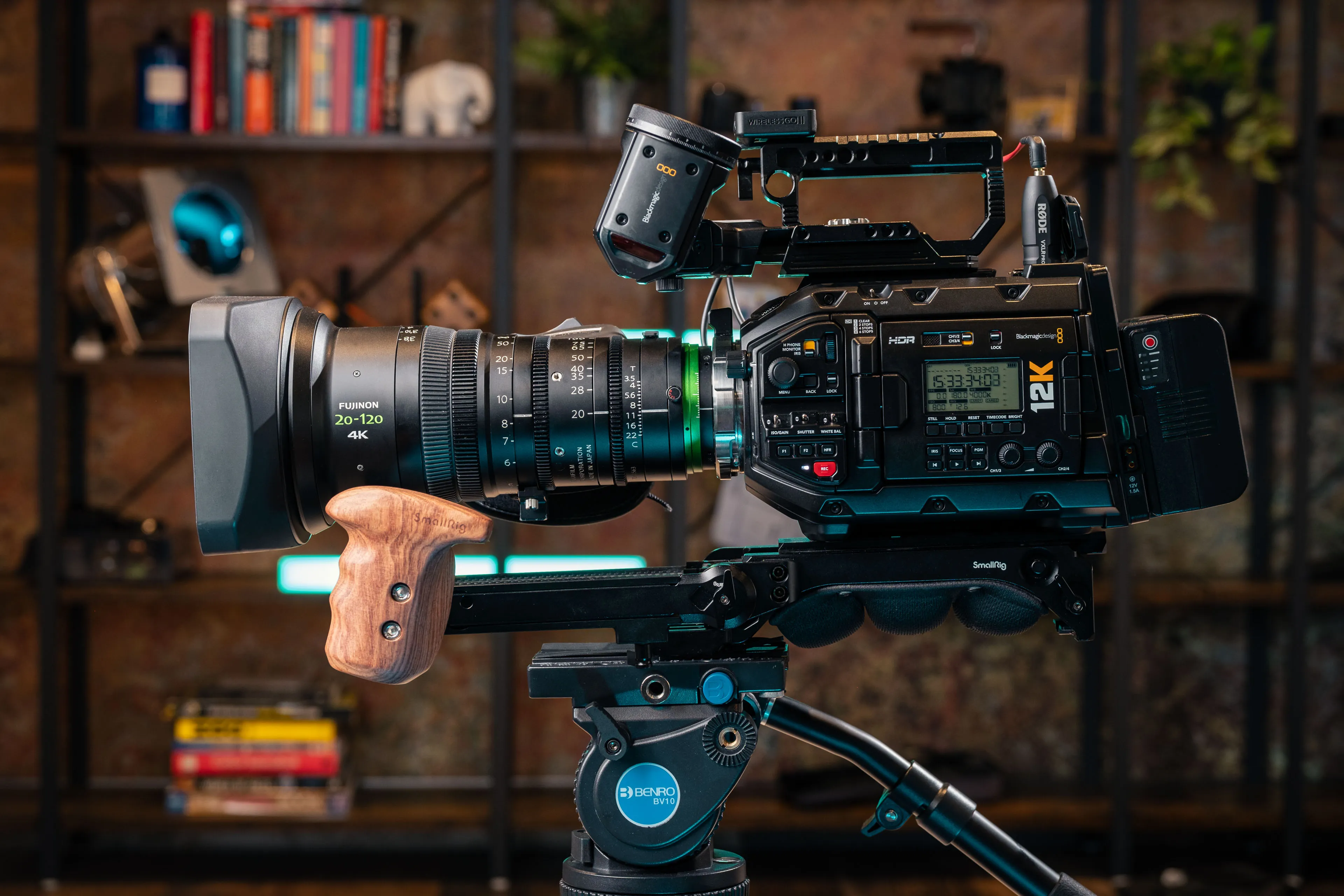 A professional 12K video camera with a Fujinon 20-120mm lens mounted on a tripod, set against a stylish background.