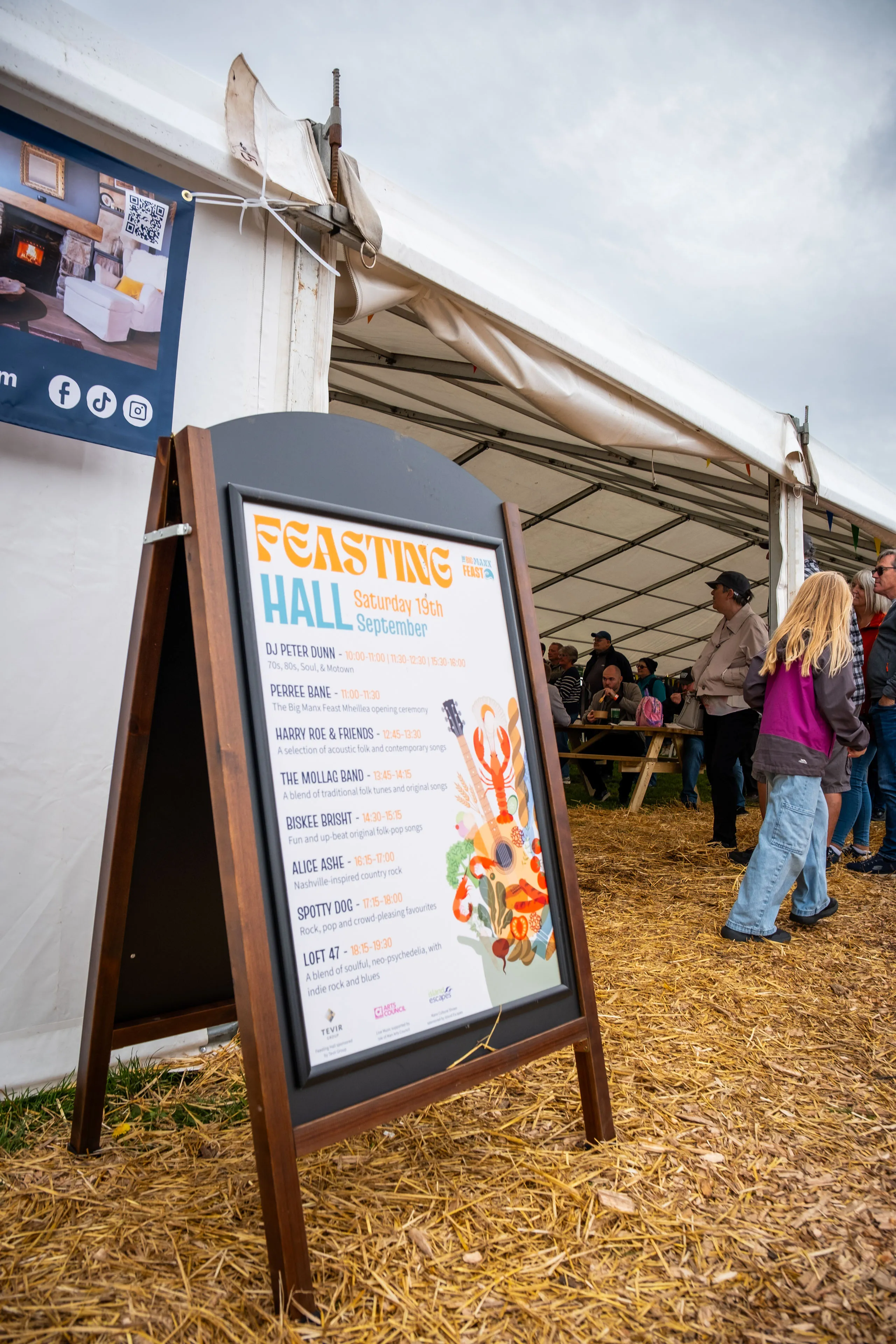 The Feasting Hall entertainment board listing Saturday's line-up, standing outside the marquee at the Big Manx Feast