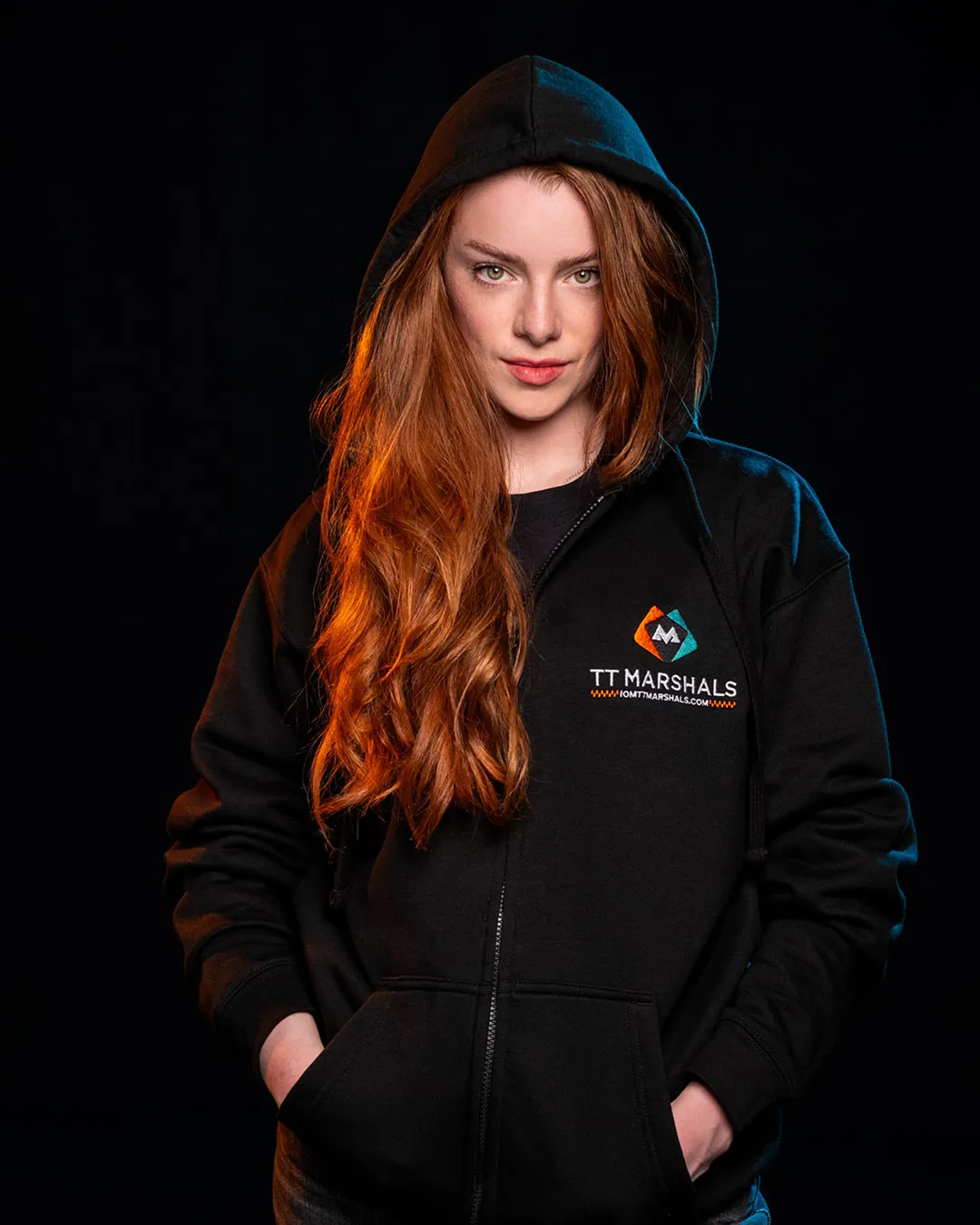 Caitlin Hampson wearing the official TT Marshals 2026 black zipped hoodie, featuring the TT Marshals logo. Exclusive marshal merchandise for the Isle of Man TT 2026.