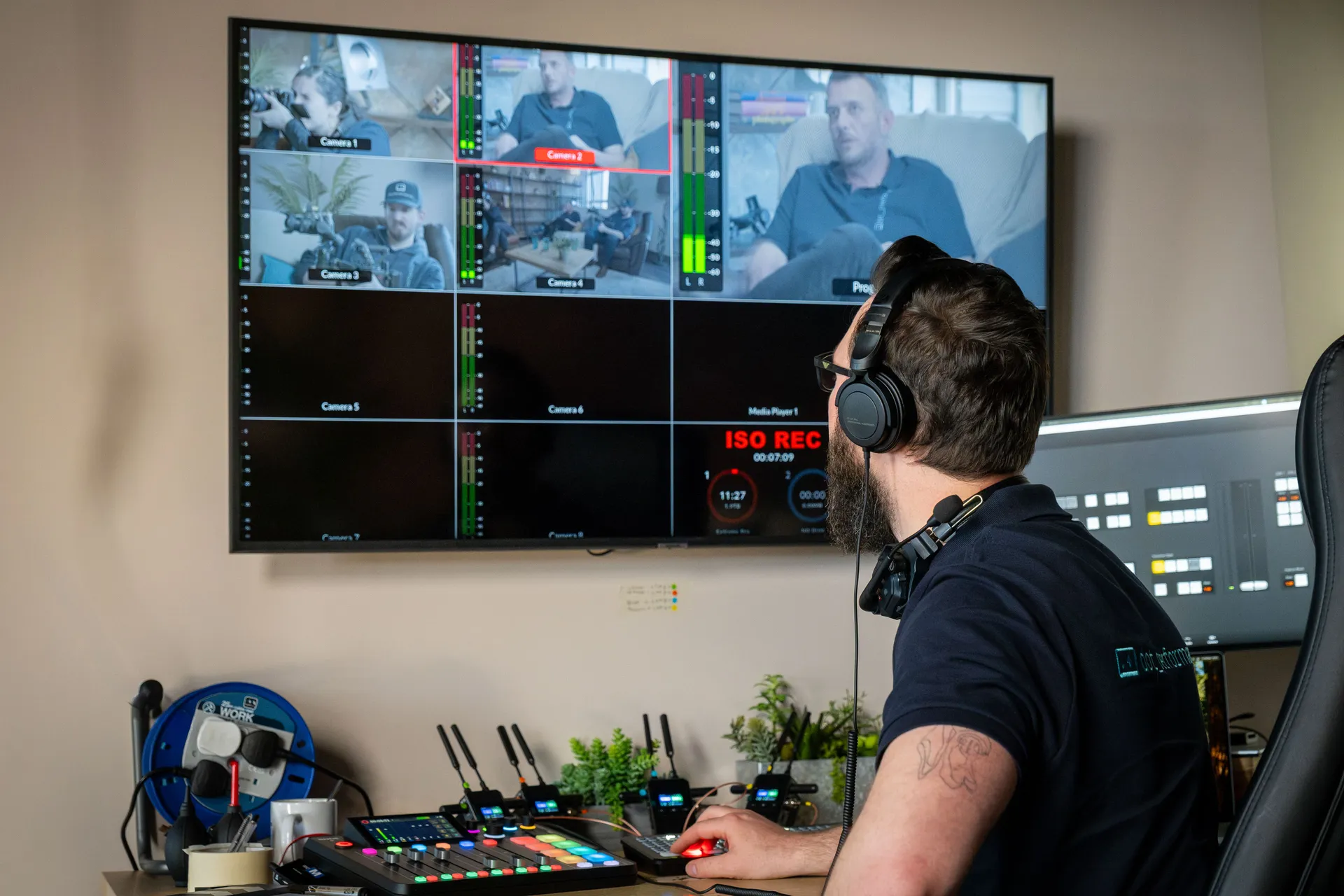 Nico van Loggerenberg operating a live video switcher (ATEM) and multi-camera monitor at the Isle of Man studio, with four camera feeds and ISO recording visible on screen,.