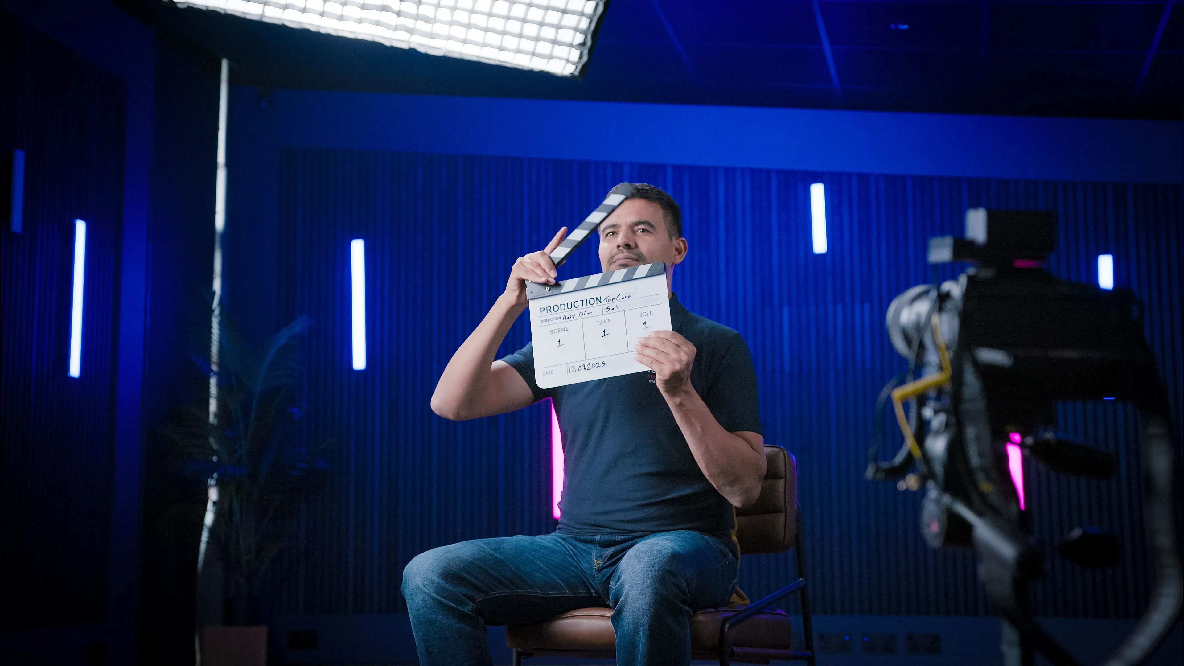 Sal Heddi holding a production clapperboard on set at DotPerformance studios, with director Andy Orton credited on the slate and cinema lighting visible in the background