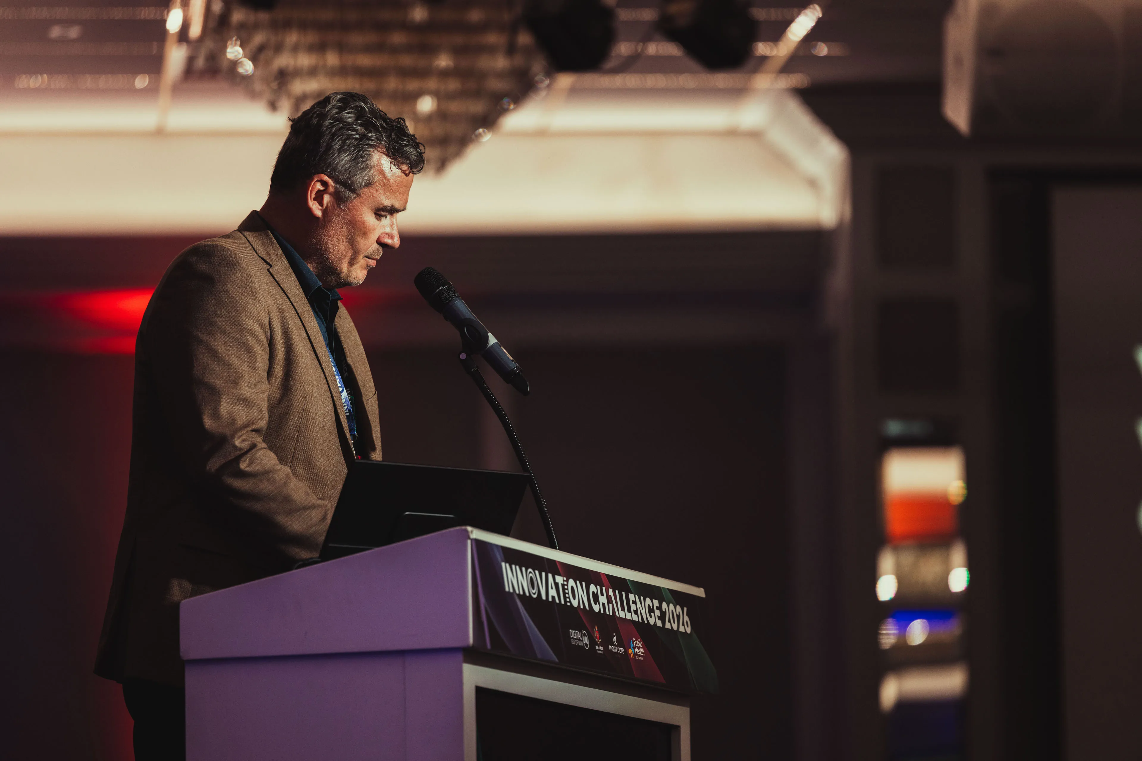 A finalist in a brown blazer speaking at the podium during Innovation Challenge 2026