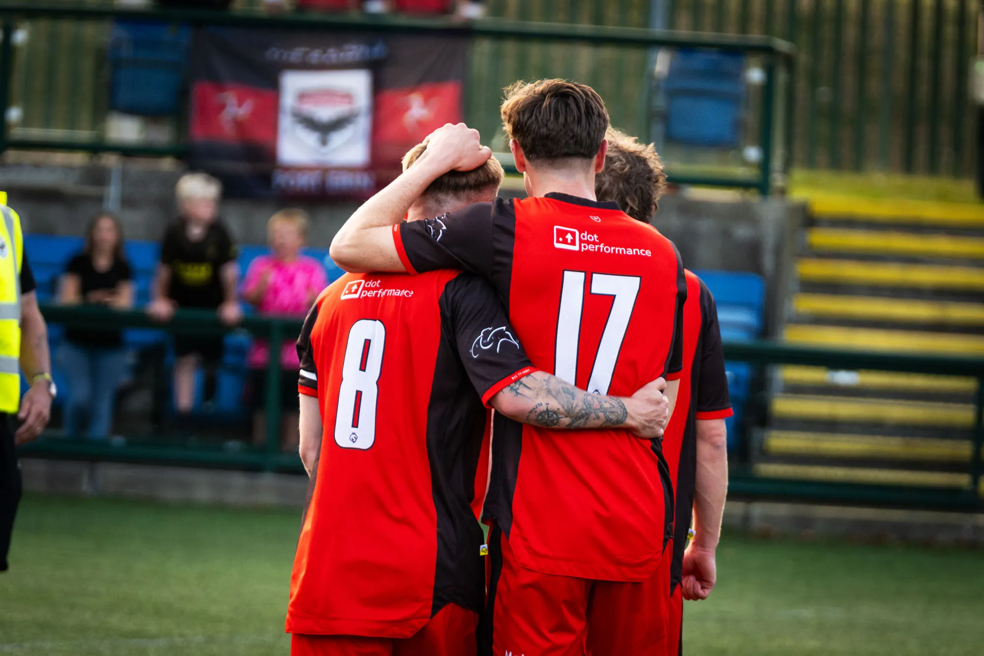 FCIOM players embracing each other on the pitch, wearing shirts branded with DotPerformance on the back
