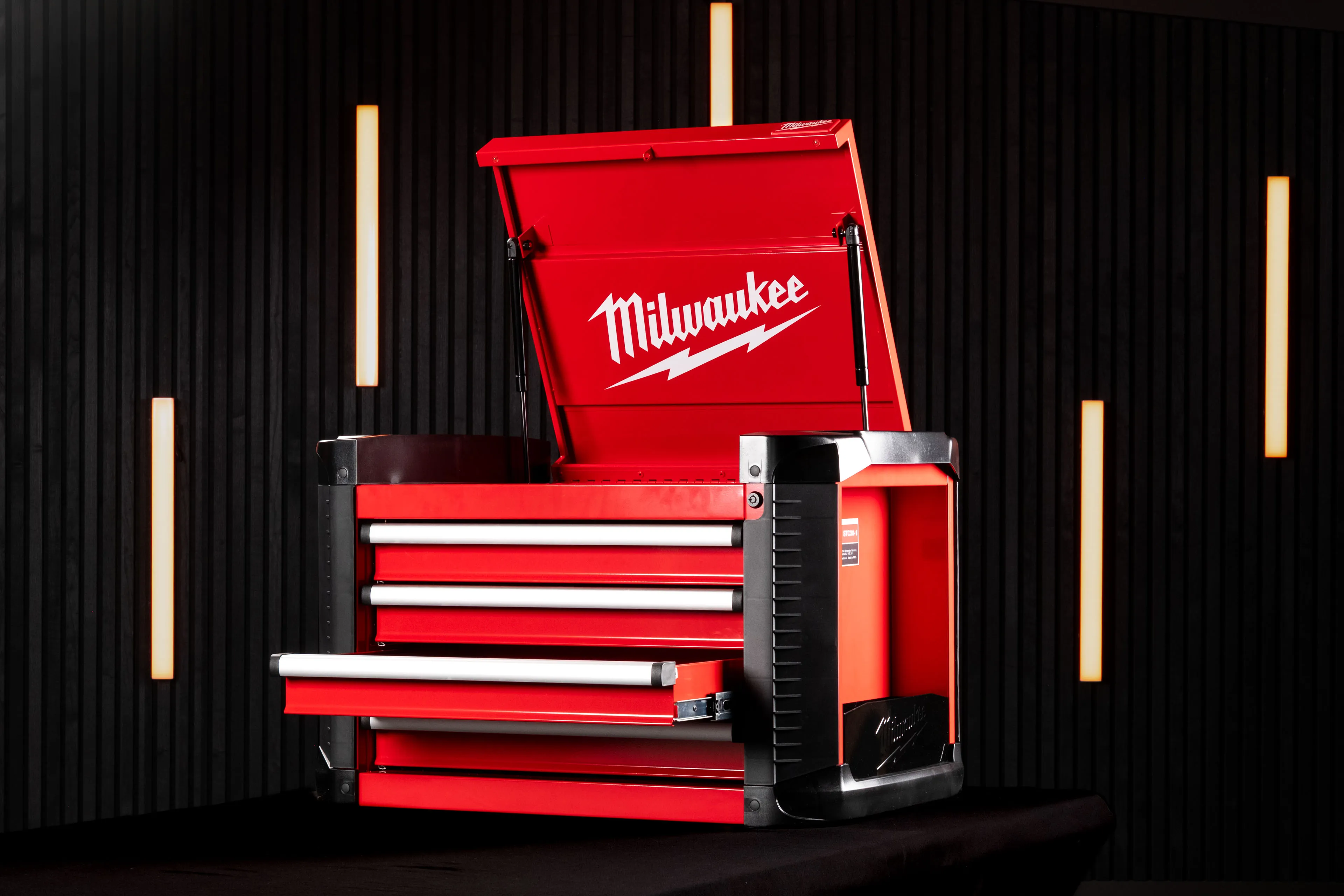 Wide shot of the Milwaukee STC30-1 Toolbox with the top lid raised and a drawer open, set against a dark studio backdrop with warm accent lighting