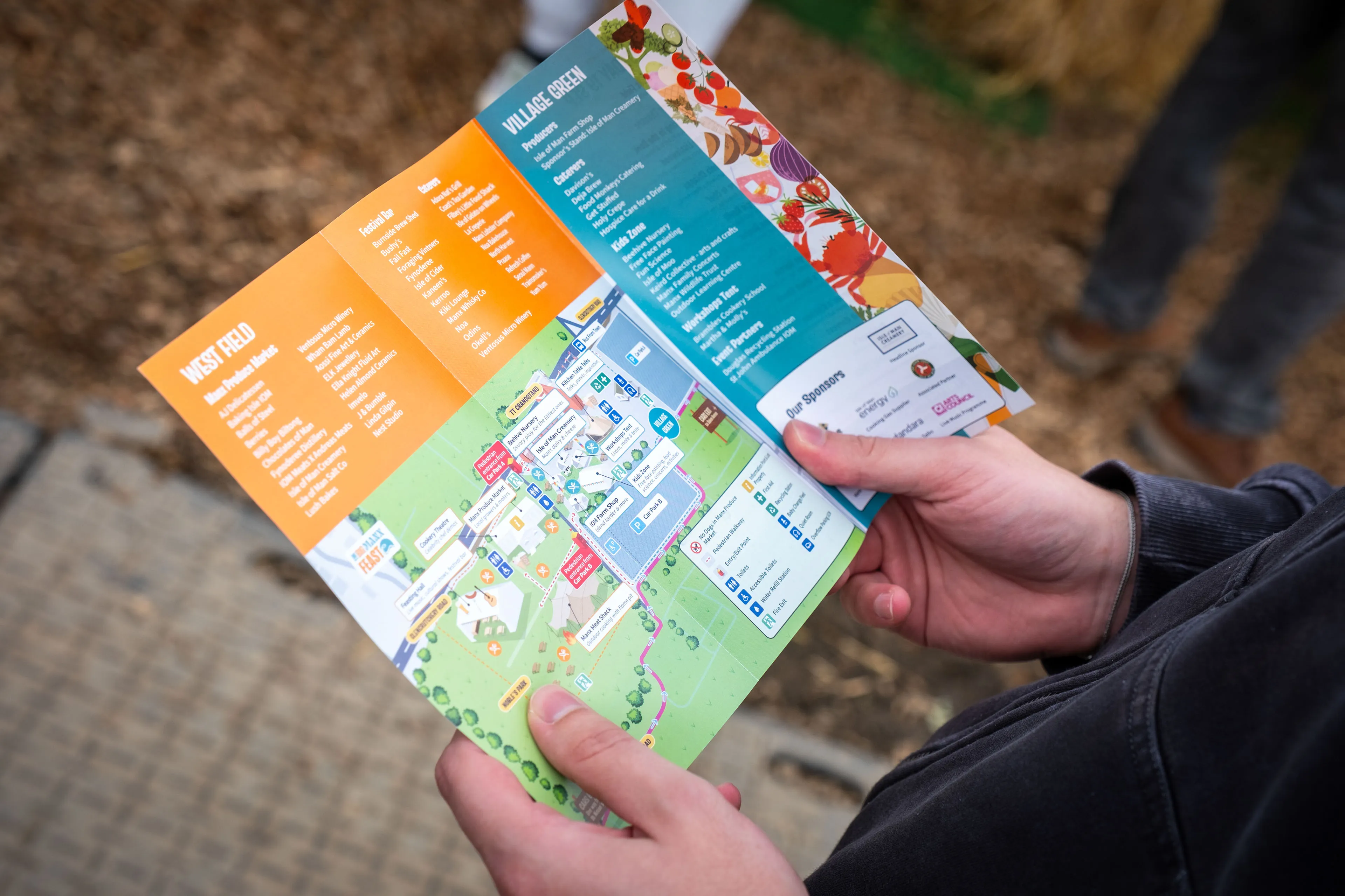 A visitor holding the Big Manx Feast consumer pamphlet, showing the site map, stallholders and Village Green listings