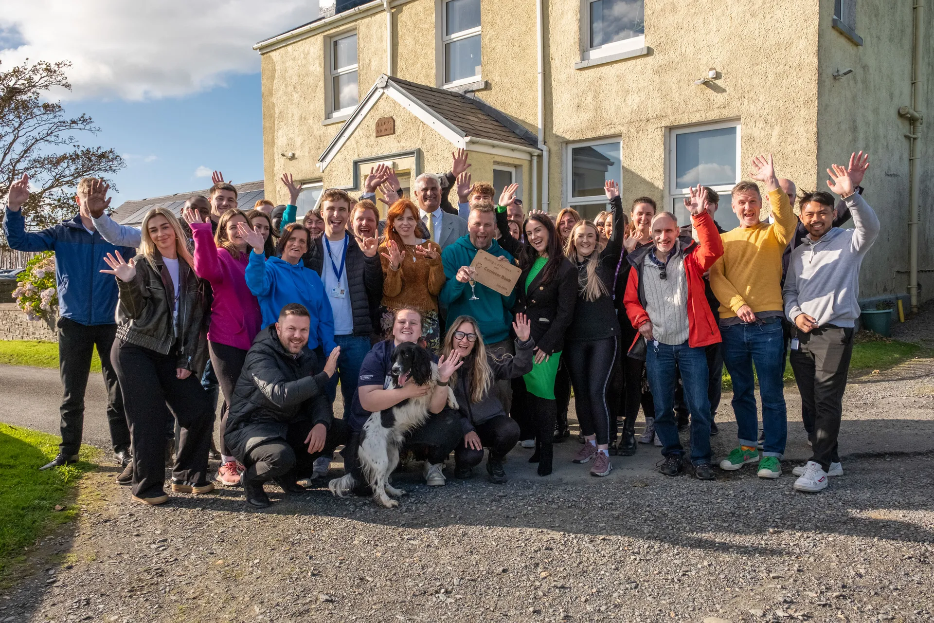 The full Conister Bank volunteer team gathered outside The Children's Centre, Isle of Man, at the end of their volunteer week filmed by DotPerformance