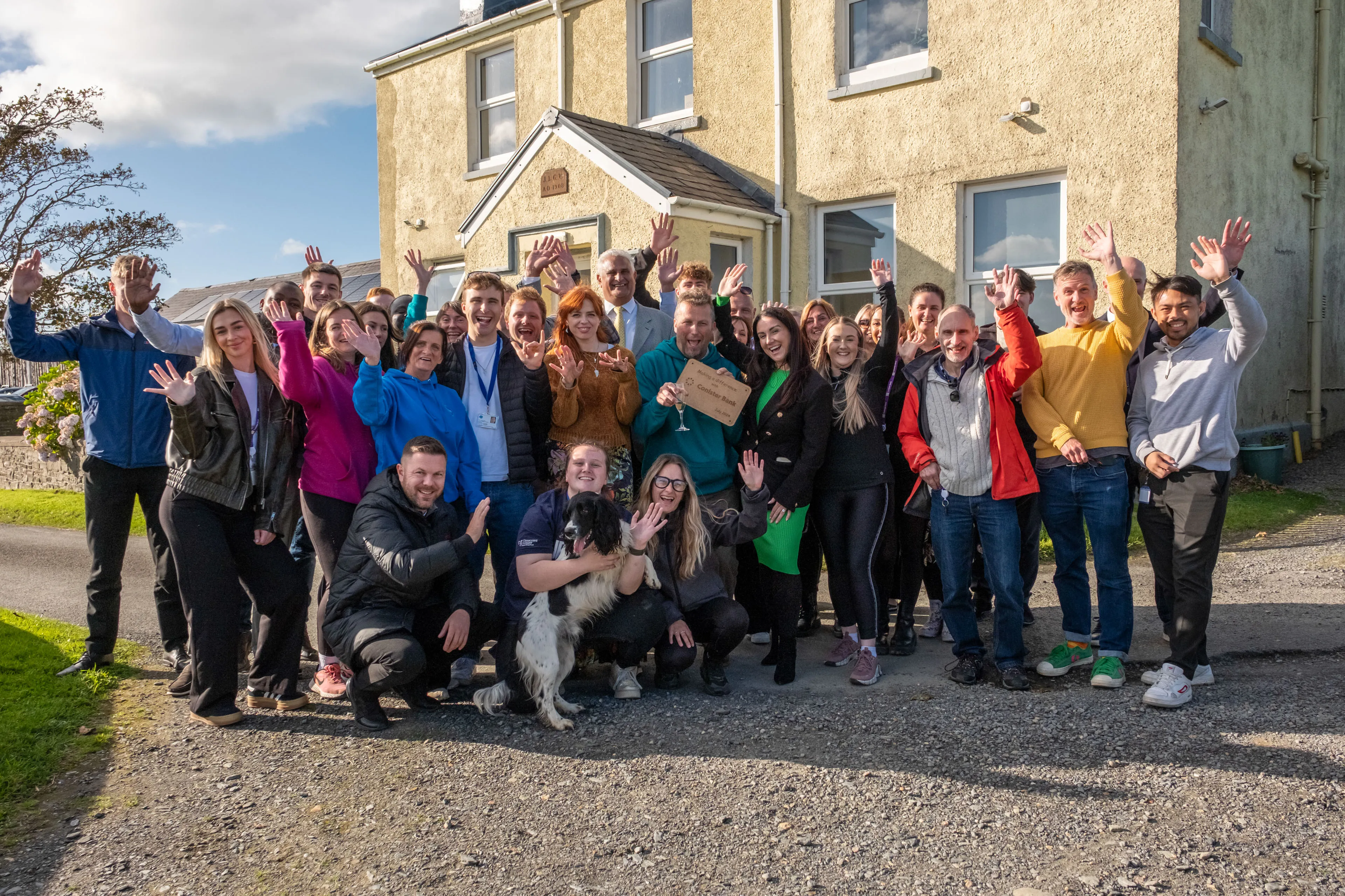 The full Conister Bank volunteer team gathered outside The Children's Centre, Isle of Man, at the end of their volunteer week filmed by DotPerformance