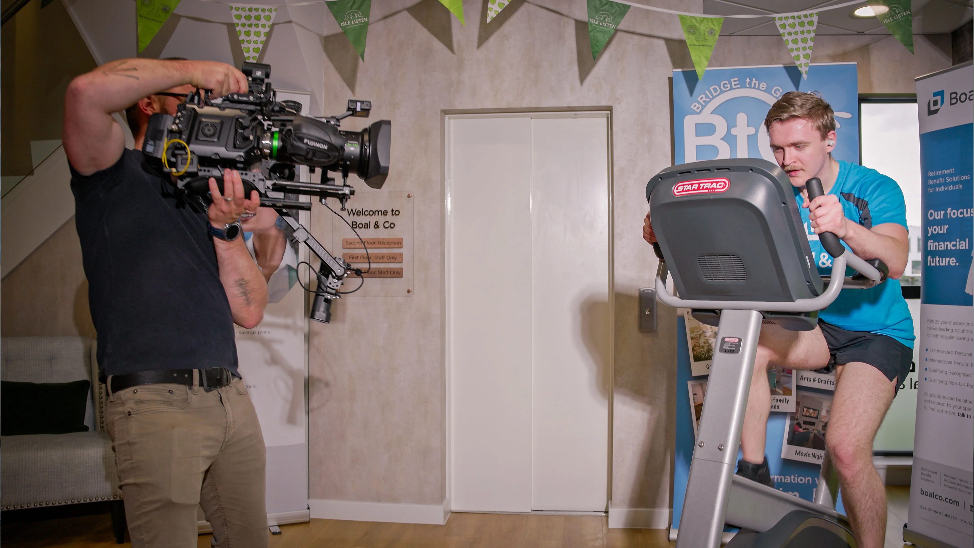 Nico van Loggerenberg from DotPerformance filming a Boal & Co team member on a static bike with a Blackmagic URSA 12K Mini Pro at the Boal & Co office on the Isle of Man