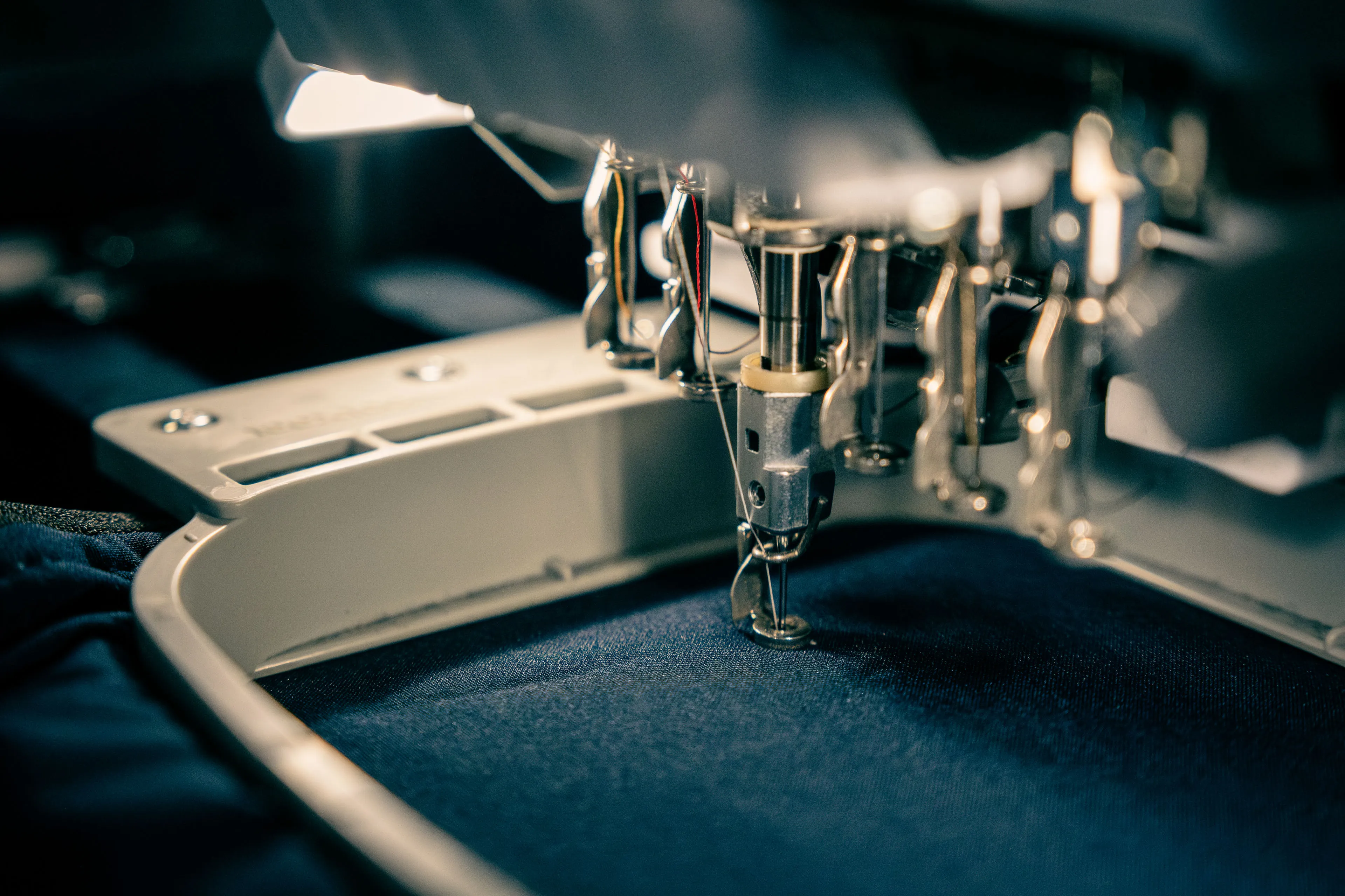 Close-up of an embroidery machine stitching on dark fabric, highlighting metallic needlework components with focused lighting, conveying precision and craftsmanship.