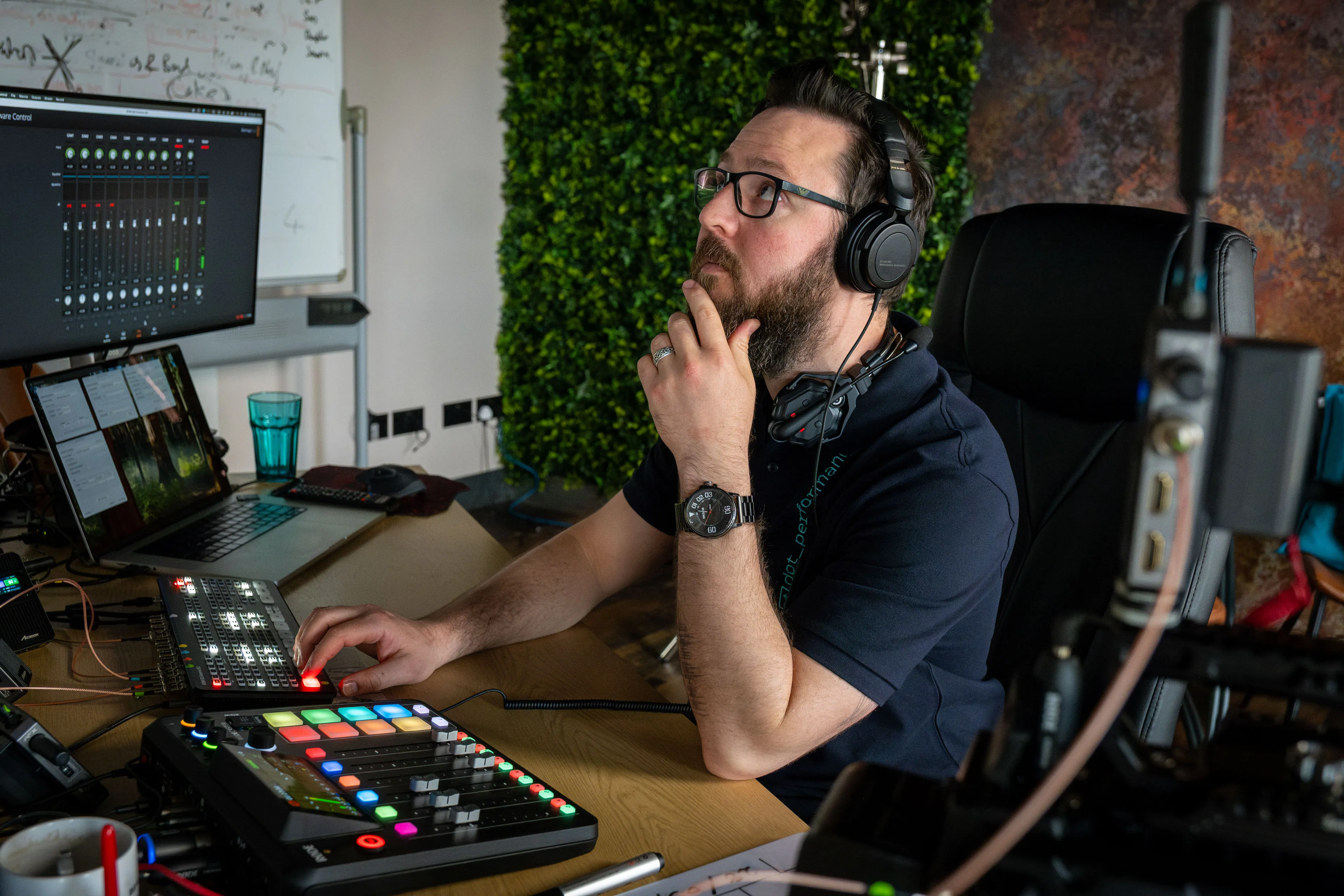 Nico van Loggerenberg wearing headphones seated at an audio and video control desk with multiple screens during a podcast production at DotPerformance studios on the Isle of Man