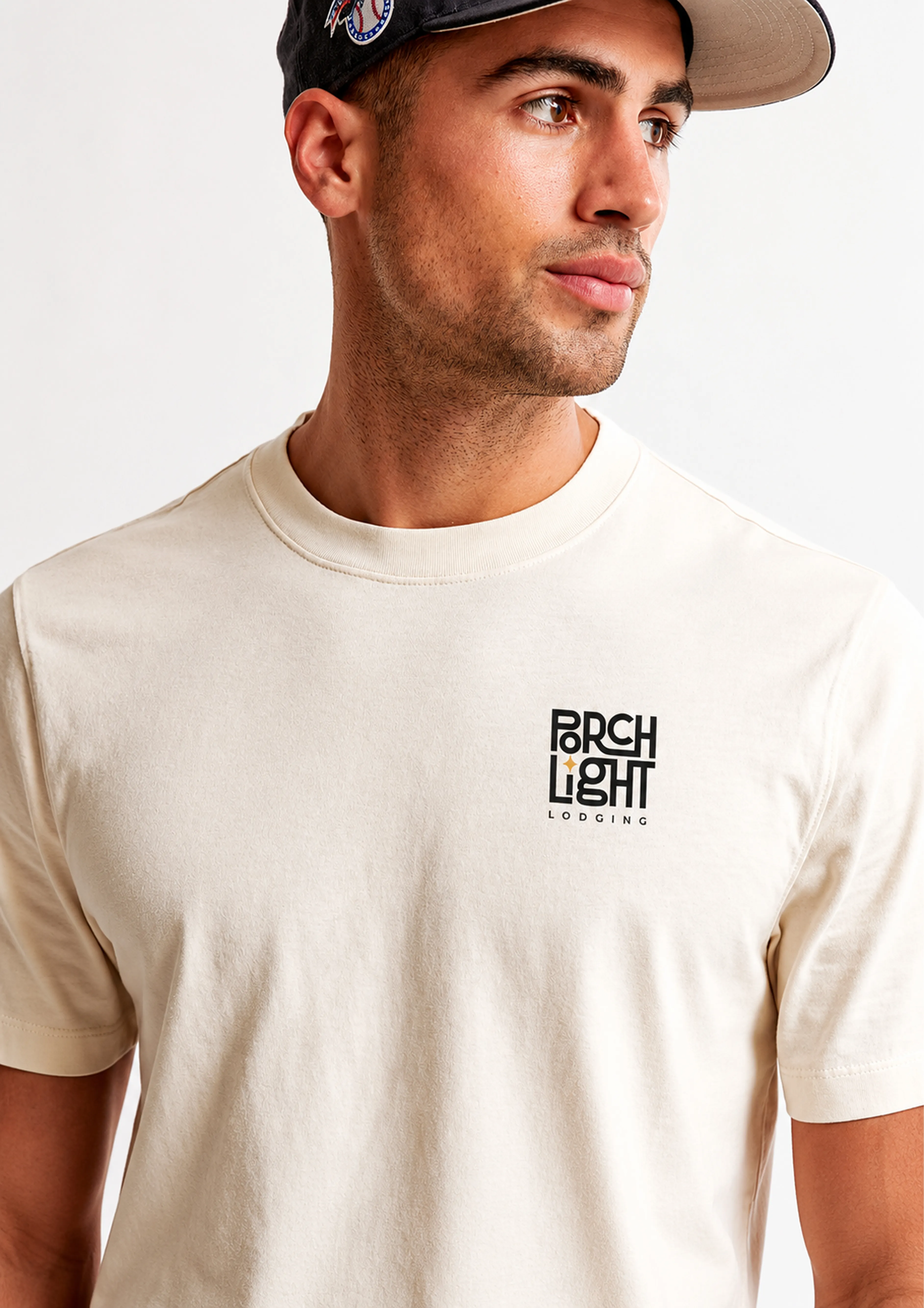 Close crop of a man in a cream PorchLight Lodging T-shirt, with the small stacked logo printed on the chest