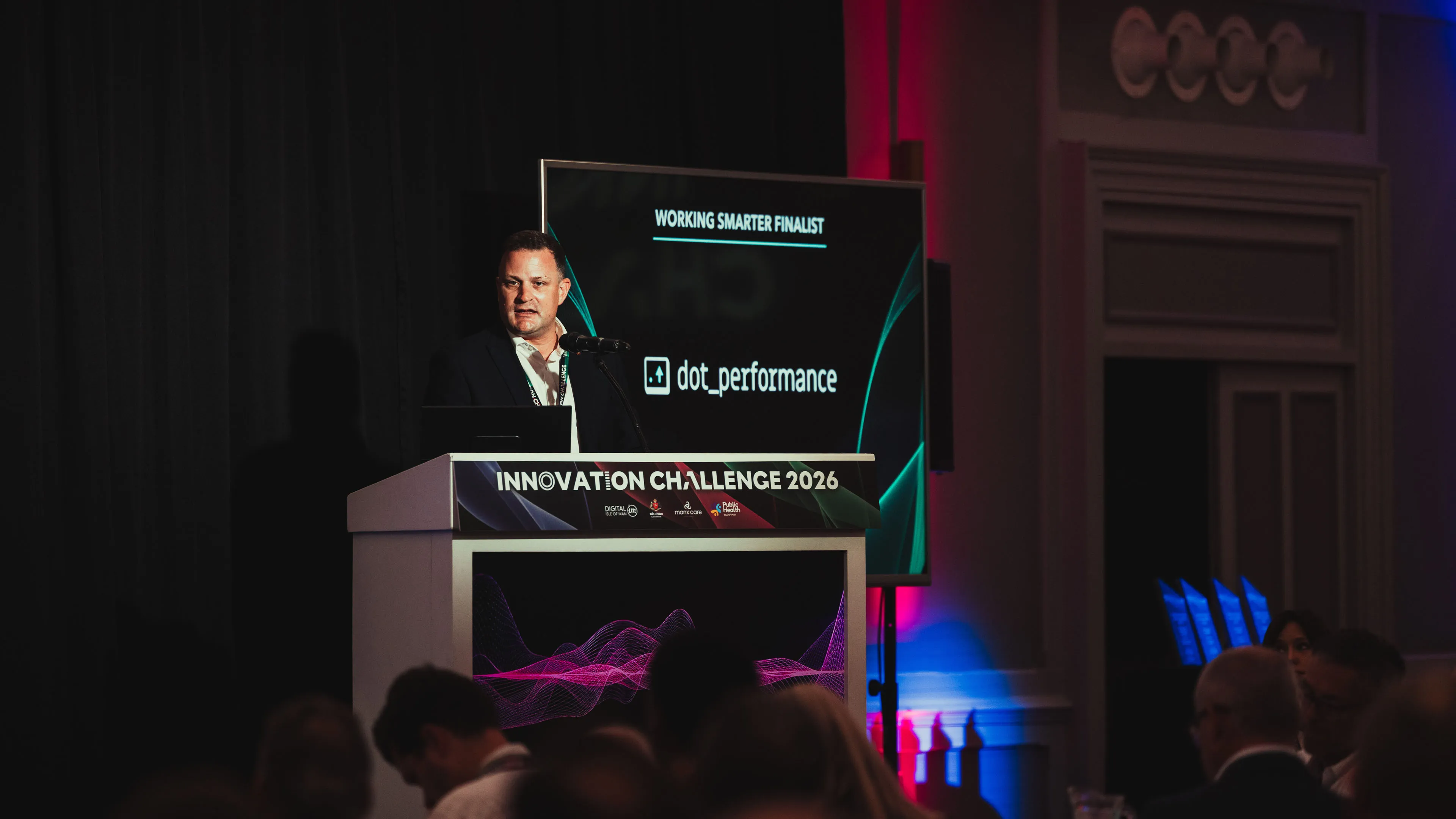 A speaker at the podium beside a "Working Smarter Finalist" screen introducing dot_performance