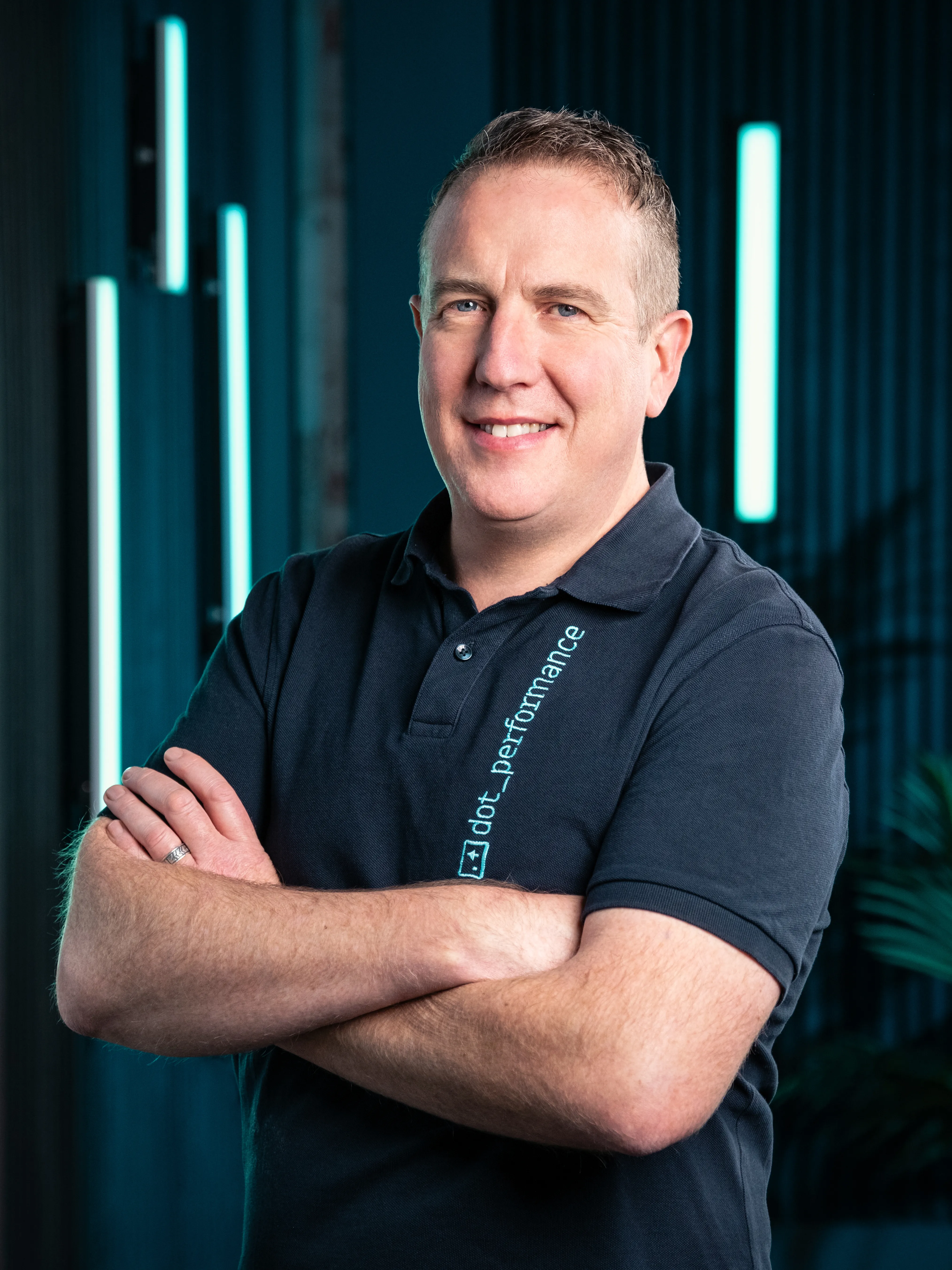 Dot Performance's Head of Digital Simon in a navy polo shirt against dark background and blue neon lights