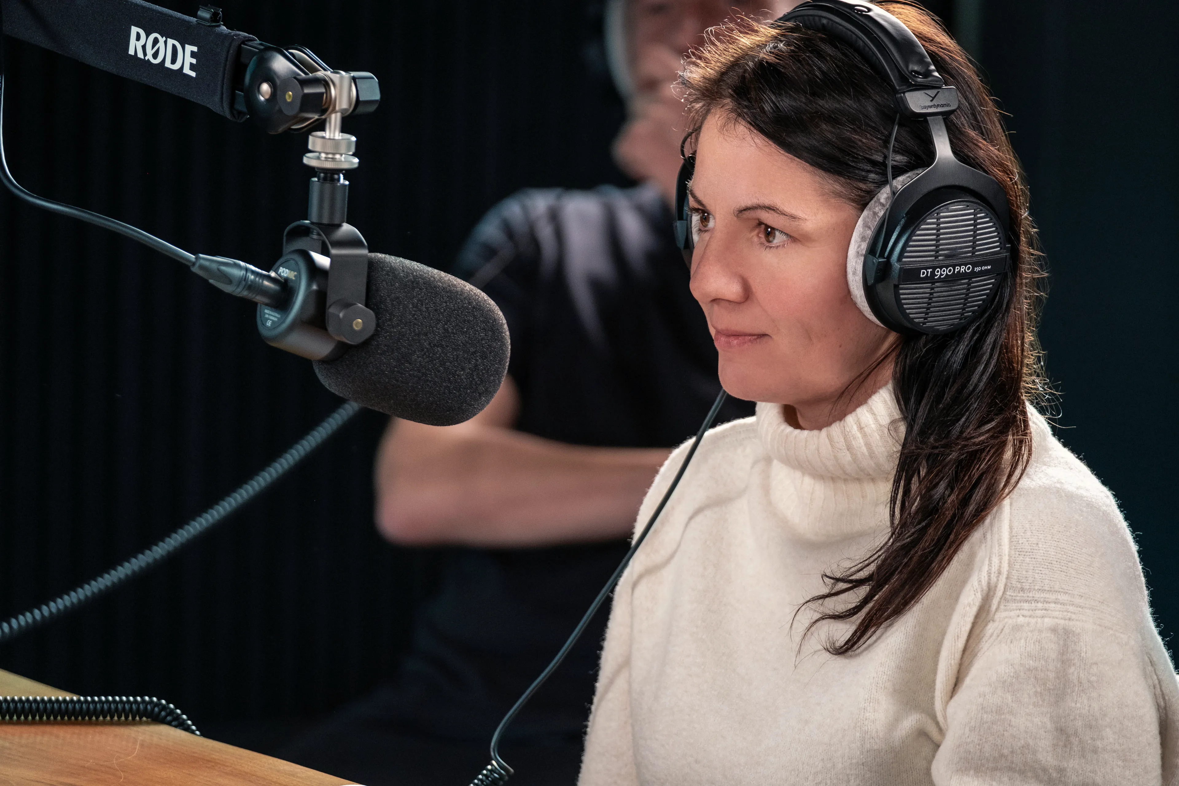 Raluca Matei Orton recording at DotPerformance studios on the Isle of Man, wearing Beyerdynamic DT 990 Pro headphones in front of a Røde podcast microphone