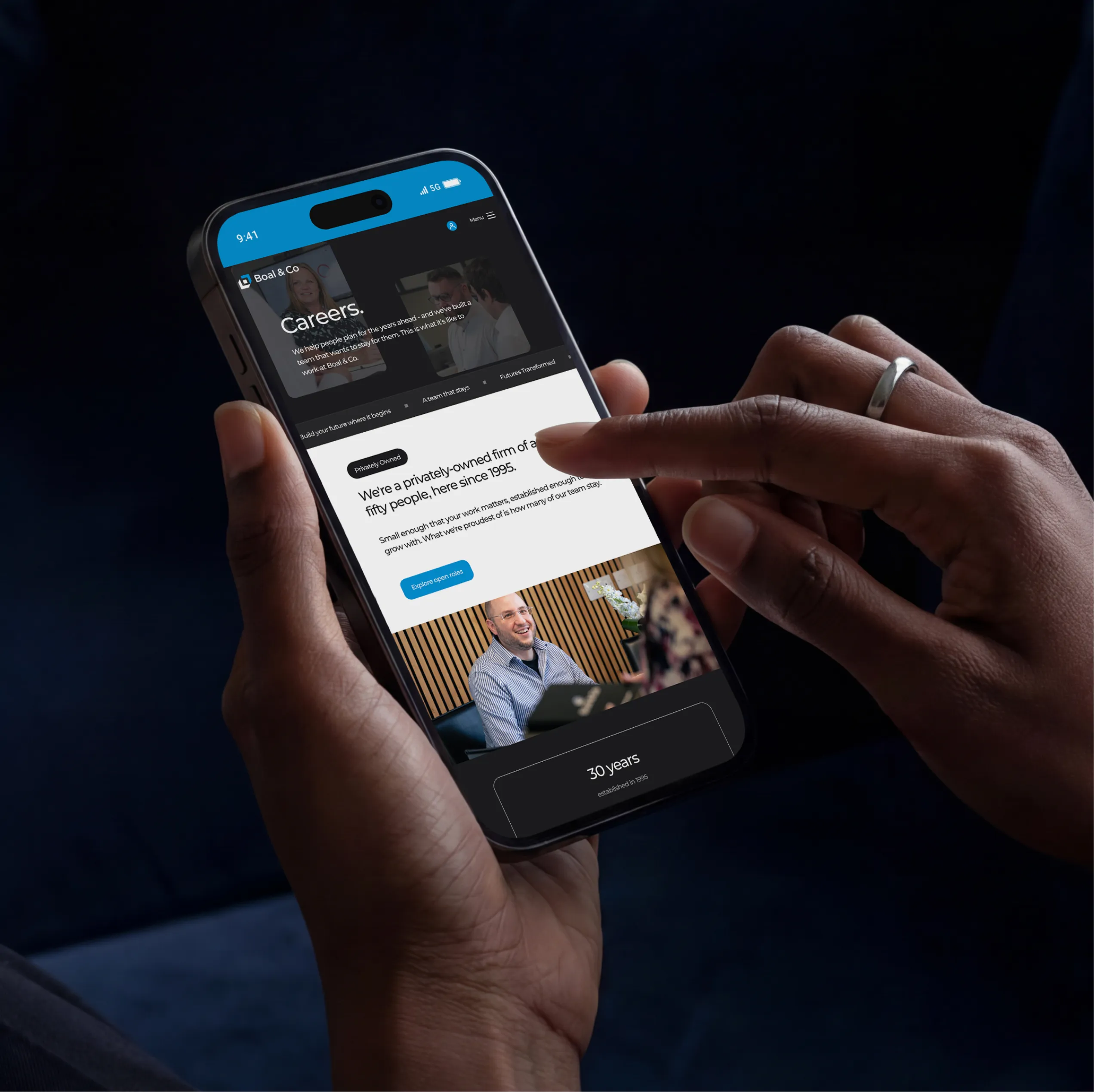 Hand holding a phone showing the Boal & Co careers page, describing a privately owned firm of around fifty people since 1995