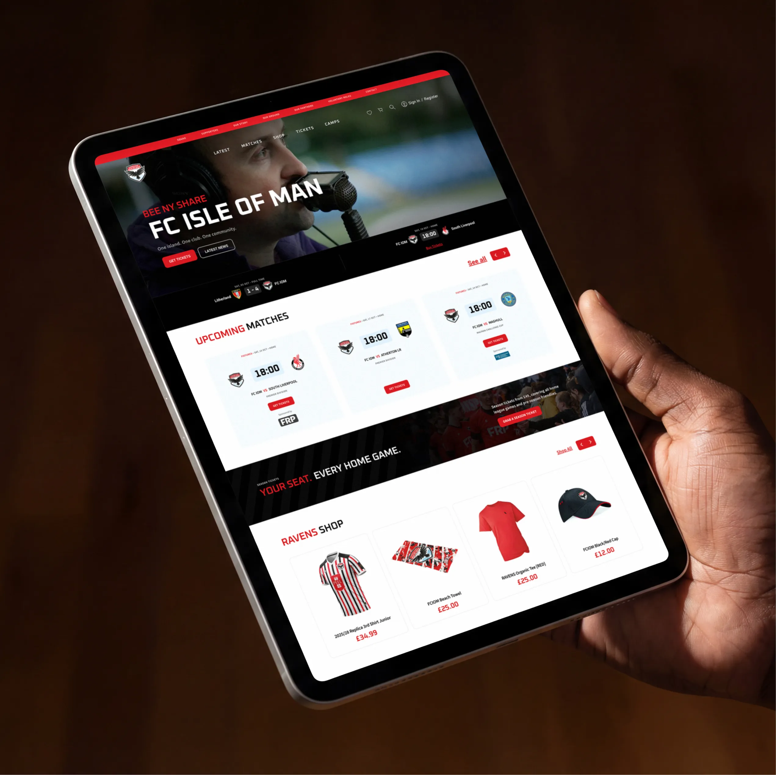 Hand holding a tablet showing the FC Isle of Man homepage, with upcoming matches, a season ticket banner and the Ravens Shop