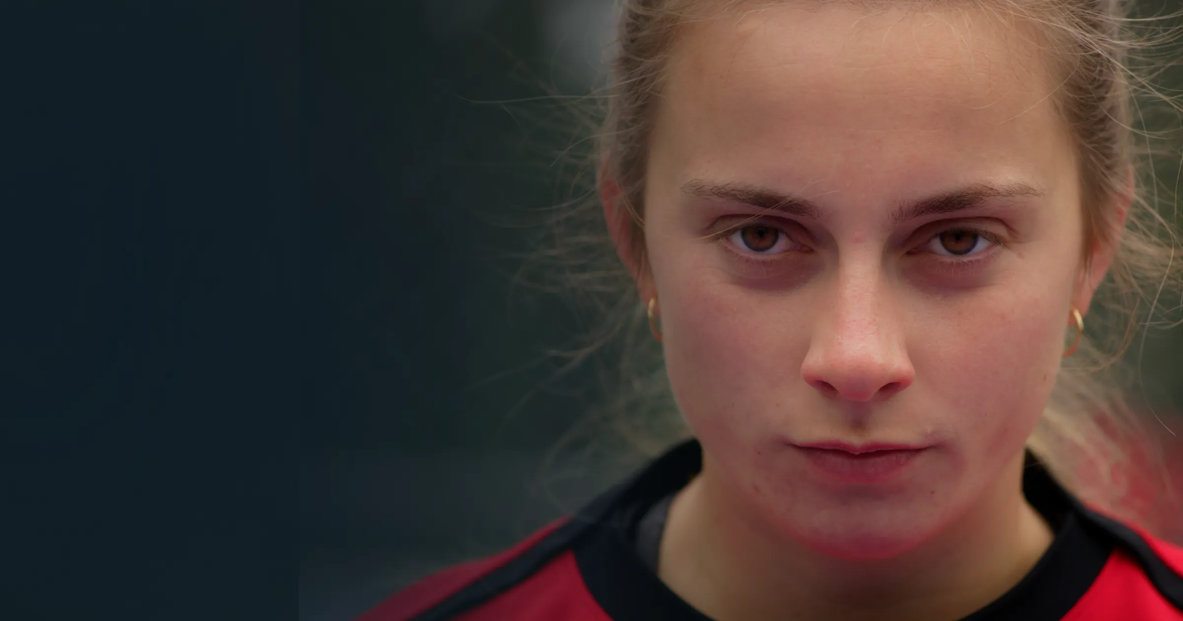 Close-up of a serious young woman in a red sports jersey conveying focus and determination.