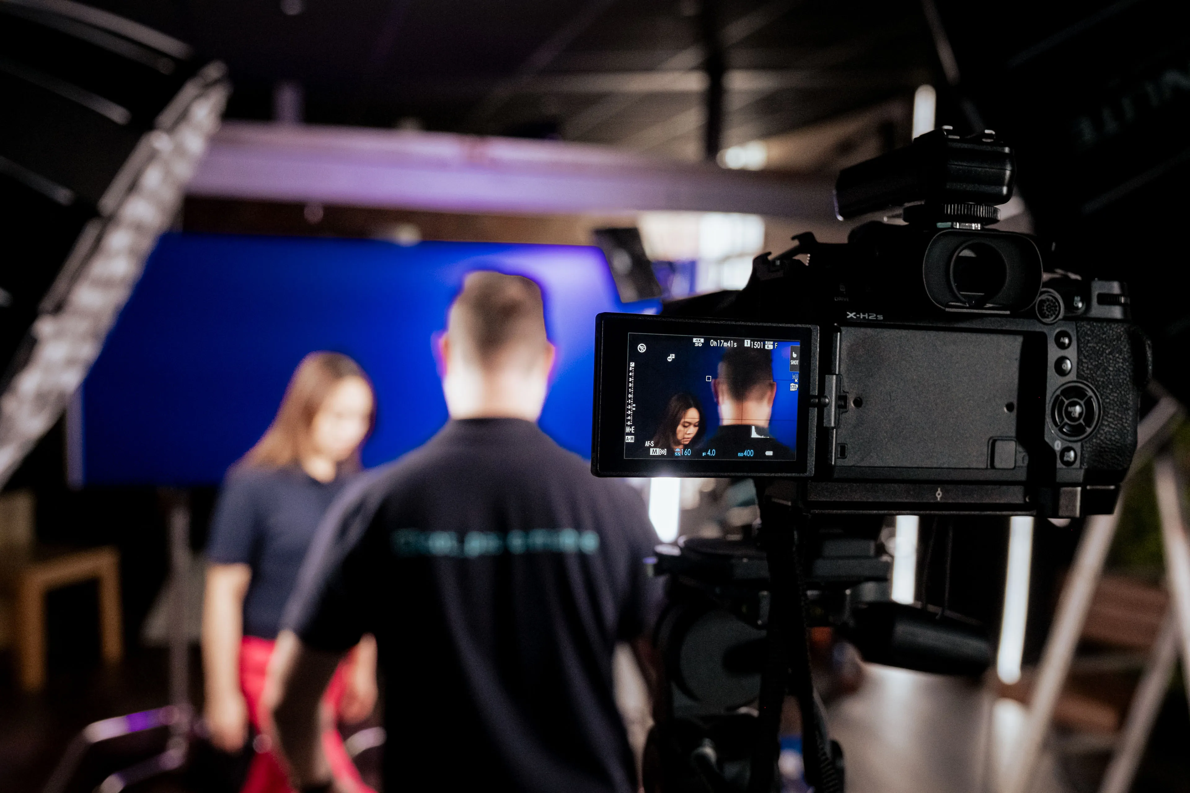 Camera monitor showing a TopCare member of staff on set during a DotPerformance photo shoot, with Nico van Loggerenberg and blue backdrop visible in the background